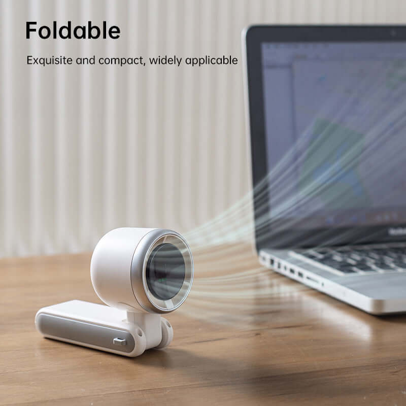 Compact white foldable electric fan for travel placed on wooden desk blowing air near laptop