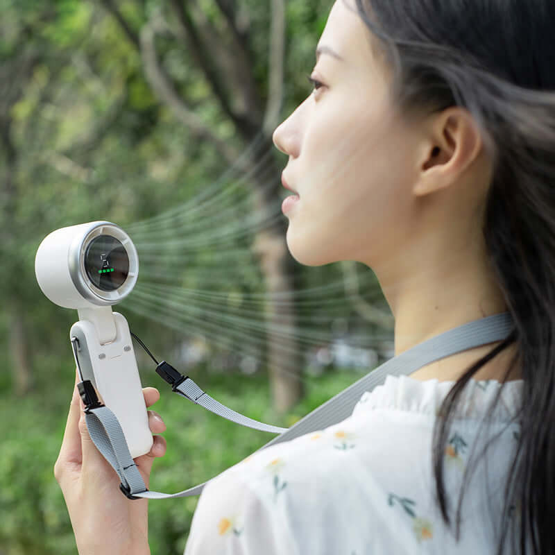 Foldable electric fan for travel held by woman outdoors with adjustable strap and sleek design