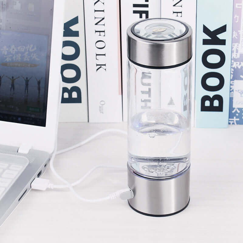 Dropshipman portable hydrogen water bottle charging next to a laptop on a white desk