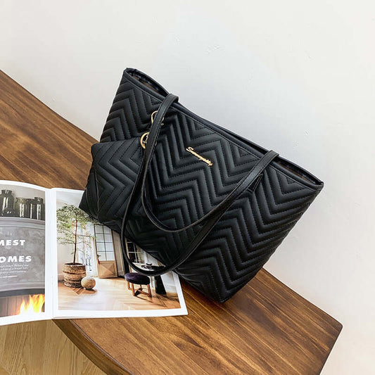 Women's Shoulder Bag with Wave Pattern Diamond Plaid Embroidery in black, exemplifying a fashionable shoulder bag style, placed on a wooden table with a magazine.