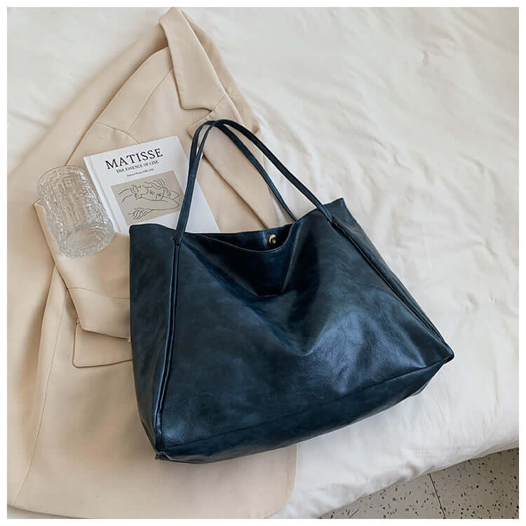 Fashion Handbag New Autumn And Winter Japanese And Korean Large Capacity Soft Leather Shoulder Bag in deep blue color placed beside a beige outfit.