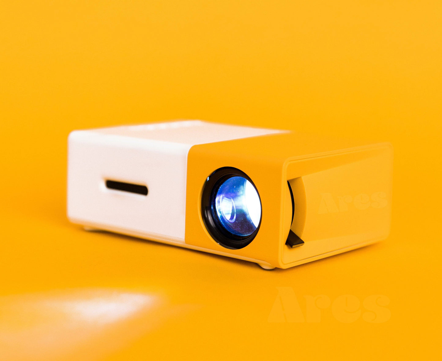 A sleek Ultra HD Mini Projector by Ecom brands displayed against a vibrant yellow background. This stylish design emphasizes its portable nature, ideal for home or outdoor entertainment. ares-projector