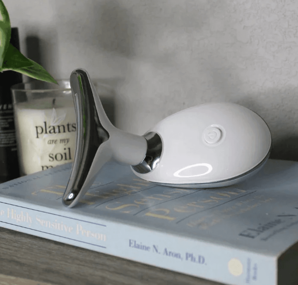 The Pure Aura Micro Glow Massager resting on a book, highlighting its aesthetic design and multifunctional use in skincare routines. A valued tool from the lumiglow, lumiglow pro series.