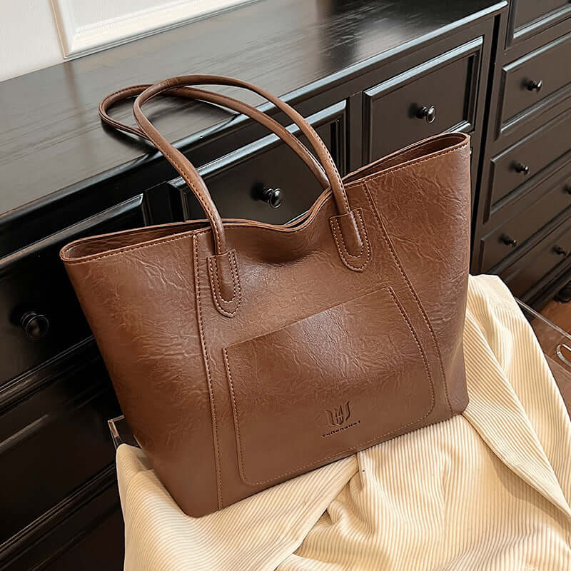 Casual Retro Shoulder Bag Texture Class Commuter Tote elegantly styled over a fabric, showcasing a medium soft tote bag in brown.
