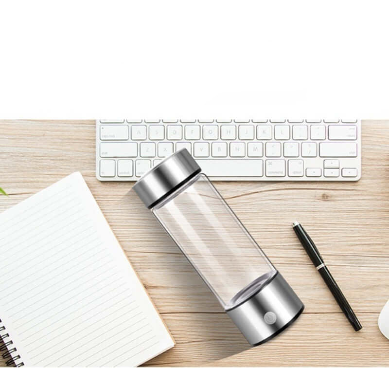 Portable hydrogen water bottle with silver lid and base placed on desk with keyboard, notebook, and pen