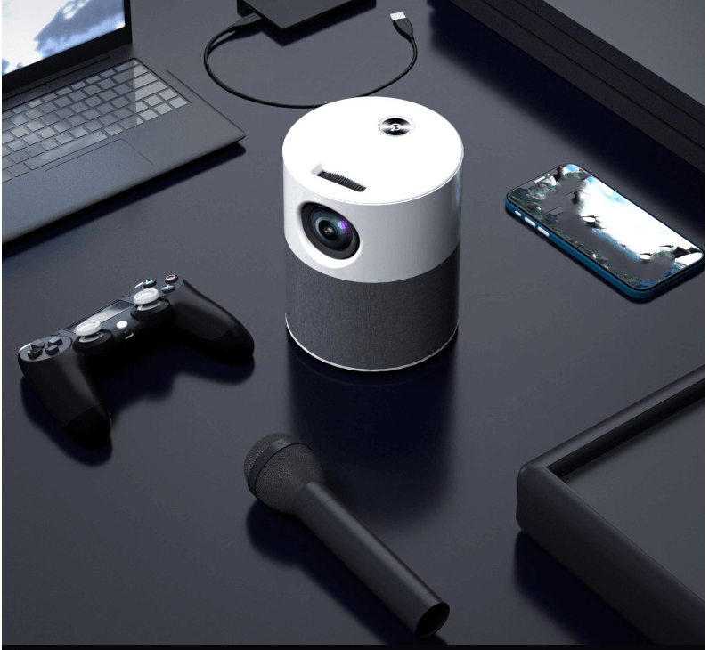 Portable mini projector for home placed on a desk with laptop, game controller, microphone, and smartphone