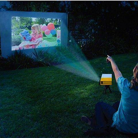 An outdoor scene featuring the Ultra HD Mini Projector by Ecom brands projecting images onto a screen while people enjoy a movie night, demonstrating its versatility for any setting. ares-projector