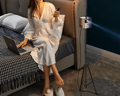 Smart projector for living room projecting on wall with woman using remote and laptop on bed